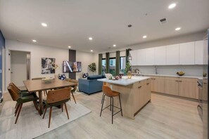 Eine moderne Küche mit Kochinsel, Essbereich mit Stühlen und Wohnbereich mit Sofa und Fernseher.
