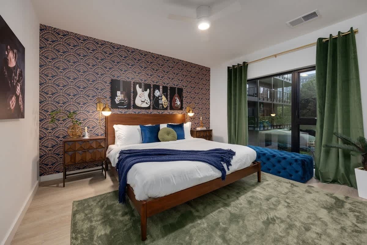 A bedroom with a bed, nightstands, a wall with artwork, a window with curtains, and a view of the outside.