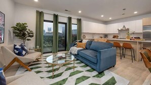 Una sala de estar moderna con sofá, mesa de centro y vistas a la ciudad a través de amplios ventanales.