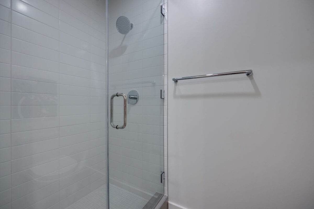 A glass-enclosed shower with a handheld showerhead, a glass door, and a metal towel rack.