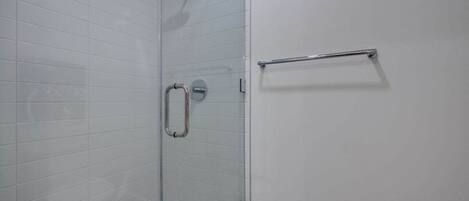 A glass-enclosed shower with a handheld showerhead, a glass door, and a metal towel rack.