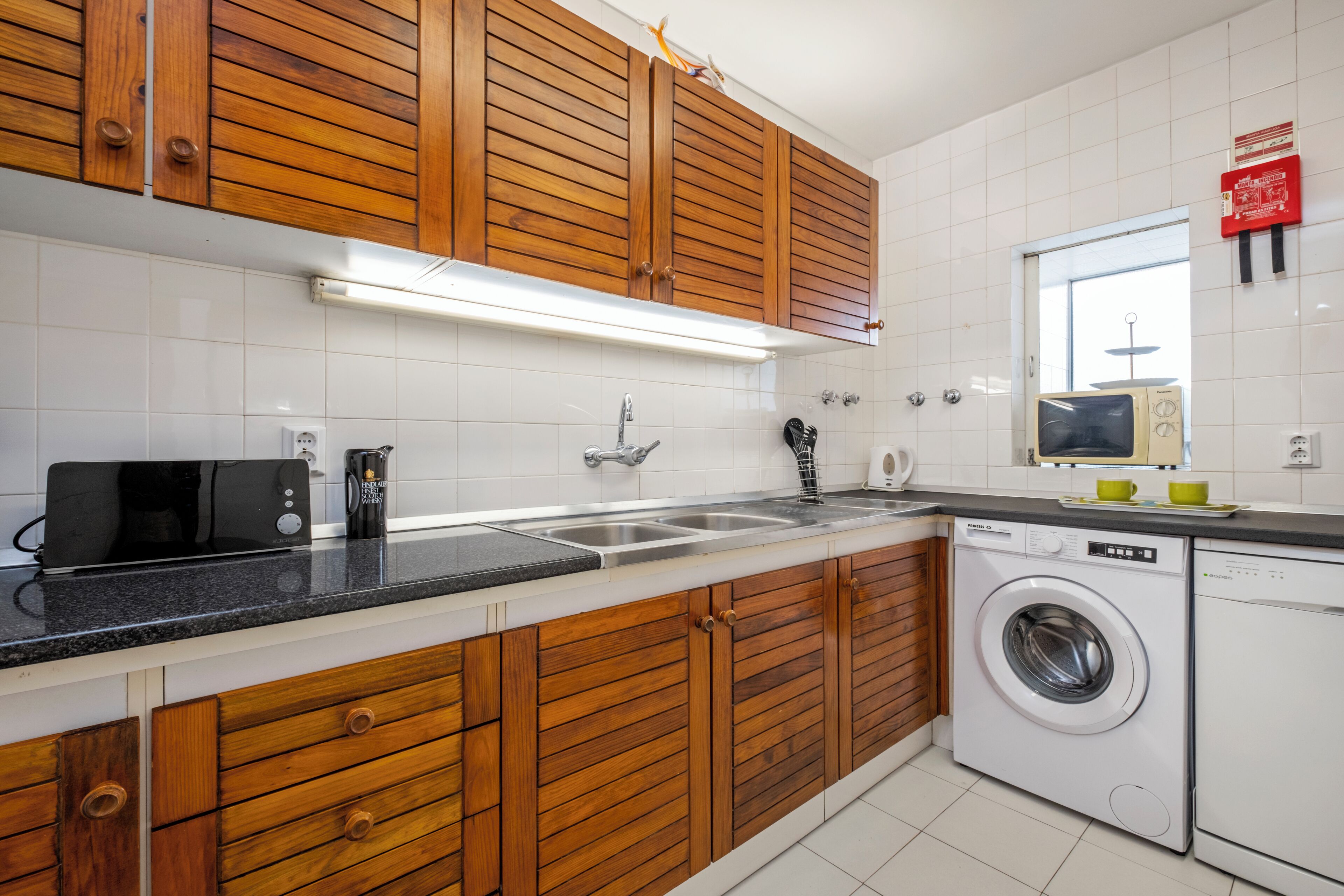 Een keuken met houten kastjes, een wasmachine en een magnetron.