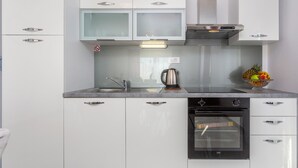 A modern kitchen with white cabinets, a stainless steel sink, a kettle, and a fruit bowl. - 2 bedroom amazing apartment in Mladenici (Mladenici)