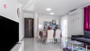 A modern living room with a flat-screen TV, a glass coffee table, a sofa, and a dining area with a table and chairs. - 2 bedroom amazing apartment in Mladenici (Mladenici)
