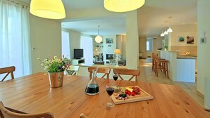 A dining area with a wooden table set for a meal, a wine bottle, and a glass of red wine. There are two pendant lights above the table.