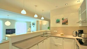 A modern kitchen with a central island, white cabinetry, stainless steel appliances, and pendant lighting.