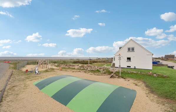 Una casa costera con una zona de playa arenosa, un tapete verde y una valla.