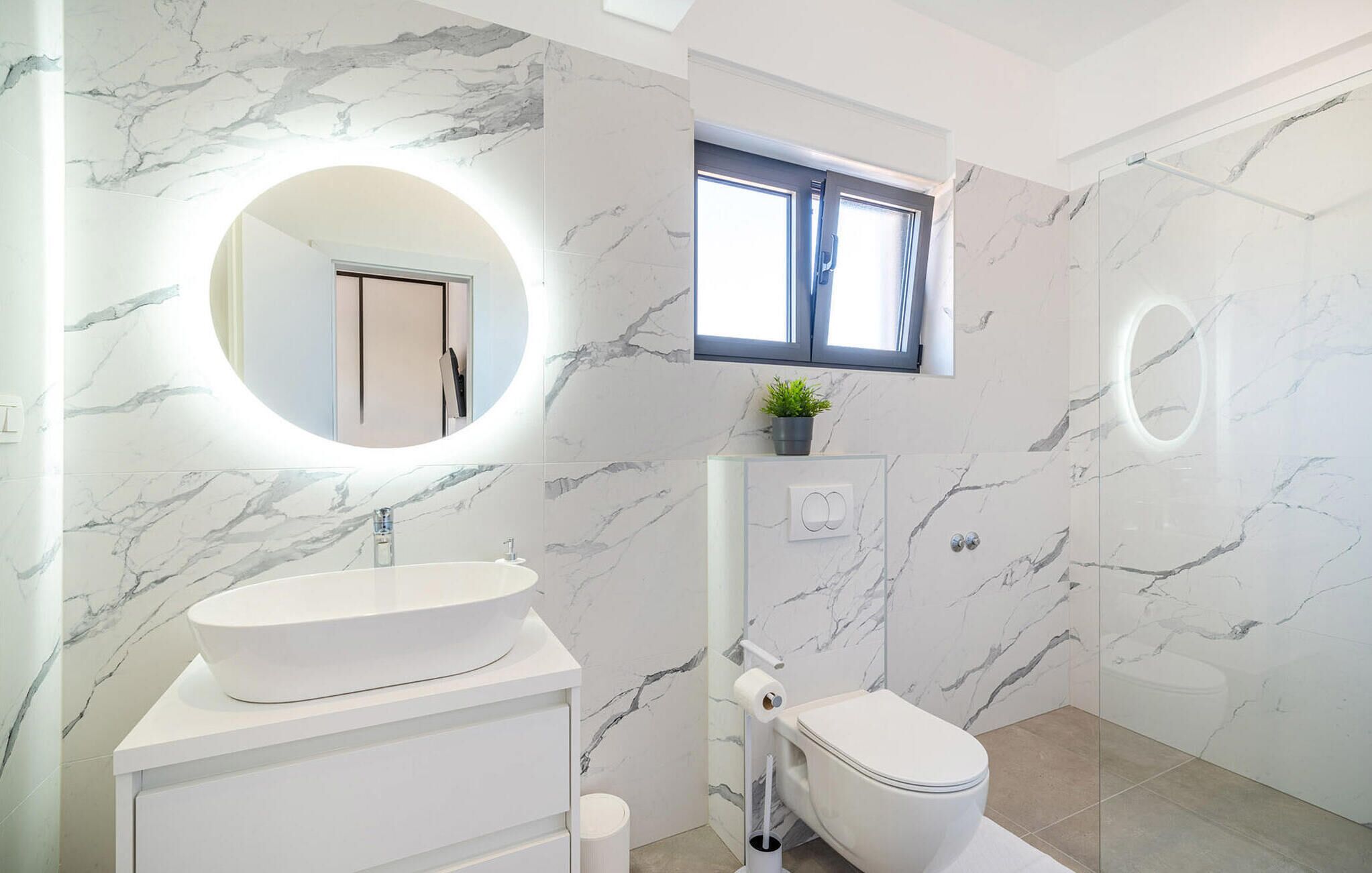 Une salle de bain avec un lavabo blanc, des toilettes et un miroir doté d’un éclairage circulaire.