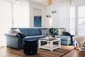 Una sala de estar con un sofá azul, una mesa de centro, una planta en maceta y una alfombra.