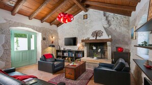 Un salon rustique avec des murs en pierres apparentes, des poutres en bois, une cheminée et un téléviseur.