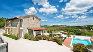 Une maison en pierre avec une piscine, entourée de verdure et sous un ciel dégagé.