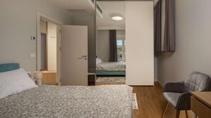 Une chambre d’hôtel avec deux lits, un bureau, une chaise et une salle de bain visible à travers une porte ouverte.