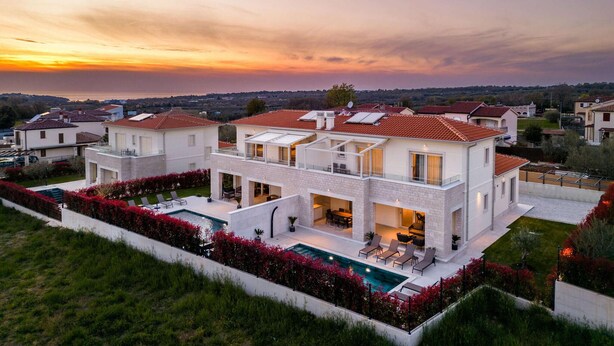 Une maison moderne à deux étages, dotée d’une piscine, de grandes fenêtres et offrant une vue sur le paysage environnant.