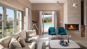 Un salon moderne comprenant un canapé, deux fauteuils turquoise, une table basse, une cheminée et un télescope, le tout près d’une porte-fenêtre coulissante donnant sur une piscine.