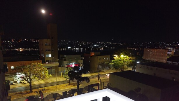 Paesaggio urbano notturno con un edificio importante, un grande cartellone pubblicitario e una strada con auto parcheggiate.
