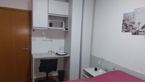 Una camera da letto con un letto, una scrivania con un computer, una sedia, un armadio e un comodino con una lampada.