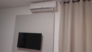 Una stanza con una TV a schermo piatto montata al muro, un condizionatore, una presa di corrente e una tenda.