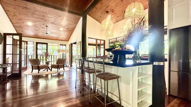 A spacious kitchen with a central island, bar stools, and a large window providing natural light. - Papillon on Coral Sea - Have you ever imagined yourself in a treehouse? (Mossman Gorge)