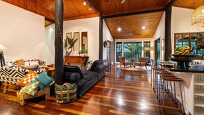 A spacious living area with a dark sofa, wooden flooring, and a ceiling fan. - Papillon on Coral Sea - Have you ever imagined yourself in a treehouse? (Mossman Gorge)