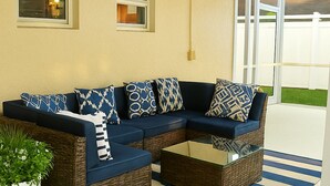 Un canapé modulable avec des coussins à motifs, une table basse en verre et un tapis rayé dans une pièce baignée de lumière naturelle, offrant une vue sur une pelouse verdoyante.