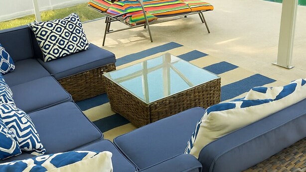 Un espace extérieur moderne, aménagé avec des canapés bleus, des coussins à motifs et une table à plateau en verre.