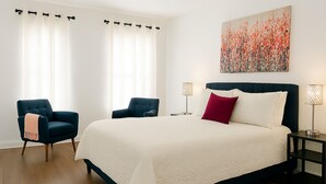 Une chambre à coucher avec un grand lit, deux fauteuils, une table de chevet avec des lampes et un tableau au mur.