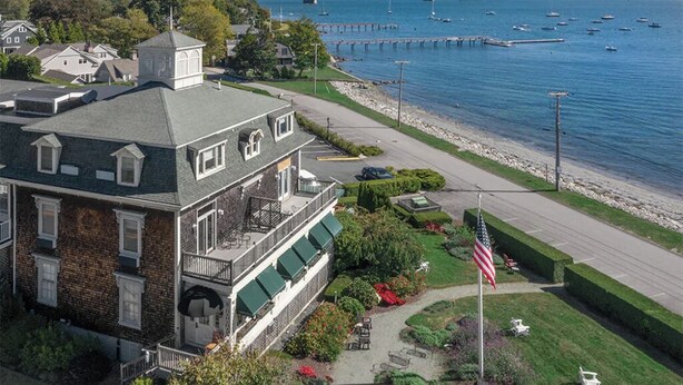 A waterfront property with a large house featuring a balcony, a flag, and a view of a bridge and boats. - 1 Bedroom Suite w/ Kitchenette, Sleeps 4, 10 min from Newport, at Voyager Inn! (Jamestown)