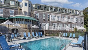 A swimming pool with lounge chairs and umbrellas, surrounded by a building with multiple windows and balconies. - 1 Bedroom Suite w/ Kitchenette, Sleeps 4, 10 min from Newport, at Voyager Inn! (Jamestown)