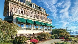 A two-story building with a balcony, green awnings, and a garden with various plants. - 1 Bedroom Suite w/ Kitchenette, Sleeps 4, 10 min from Newport, at Voyager Inn! (Jamestown)