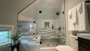 Et moderne badeværelse med en brusekabine i glas, toilet og håndvask.