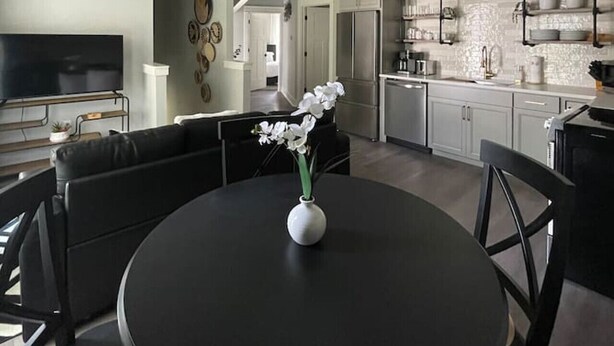 Een moderne woonkamer met een ronde zwarte tafel, witte orchideeën, zwarte leren banken en een flatscreen televisie.
