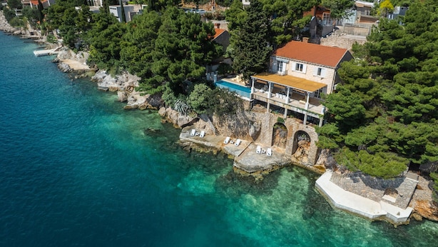 Eine Küstenimmobilie mit Pool, Liegestühlen und einer Stegbrücke.
