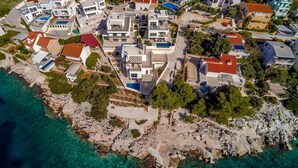 An aerial view of a coastal residential area with modern houses, clear blue waters, and rocky terrain. - 4 bedroom nice home in Razanj (Razanj)