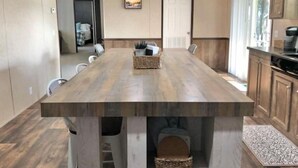 A modern kitchen with a long wooden table, built-in cabinets, and a view of the adjacent living area. - "Lost Crab", beautiful 3BR, big yard, private dock (Centre)