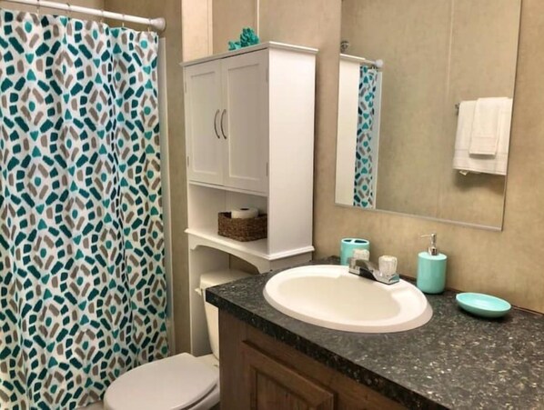 A bathroom with a white toilet, a sink with a granite countertop, a white cabinet with a mirror above it, and a shower curtain with a geometric pattern. - "Lost Crab", beautiful 3BR, big yard, private dock (Centre)