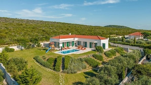 Une villa moderne dotée d’une piscine, de volets verts et offrant une vue sur les collines.