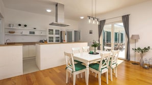 Une cuisine moderne avec des meubles blancs, un îlot central et un coin repas avec des chaises blanches et des coussins verts.