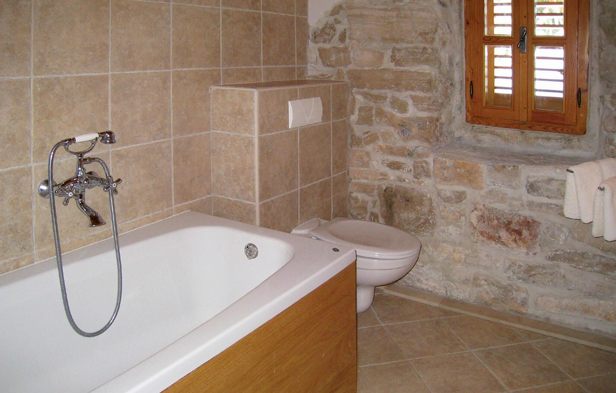 A bathroom with a bathtub, a toilet, and a stone wall.