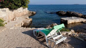 A beachside setting with a white lounge chair covered with a green towel, rocky terrain, and a calm sea in the background. - Lovely home in Orebic (Orebic)