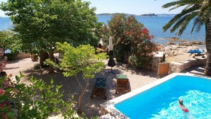 A pool area with a view of the sea, surrounded by trees and outdoor furniture. - Lovely home in Orebic (Orebic)