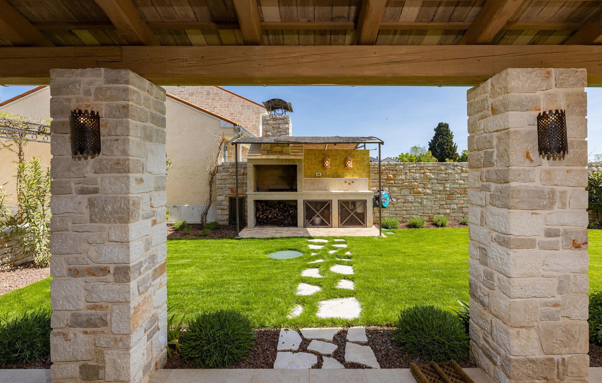 A stone patio with a stone wall and a wooden pergola overhead.
