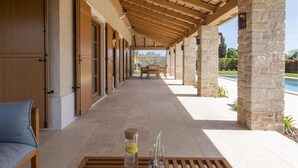 Un espacio al aire libre techado con una piscina, pilares de piedra y una mesa con una bebida y vasos.