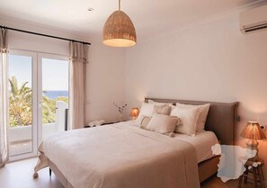 Une chambre avec un grand lit, un luminaire suspendu, une table de chevet et une vue sur l’extérieur.