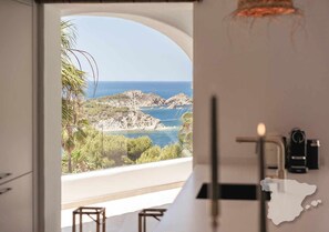 A room with a view of a rocky coastline and the sea. There is a bar area with stools and a candle on the counter. - CostaBlancaDreams - The Jave in Javea (Javea)