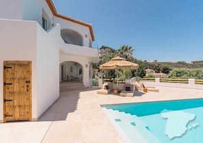 A modern villa with a pool, outdoor seating, and a view of the surrounding landscape.