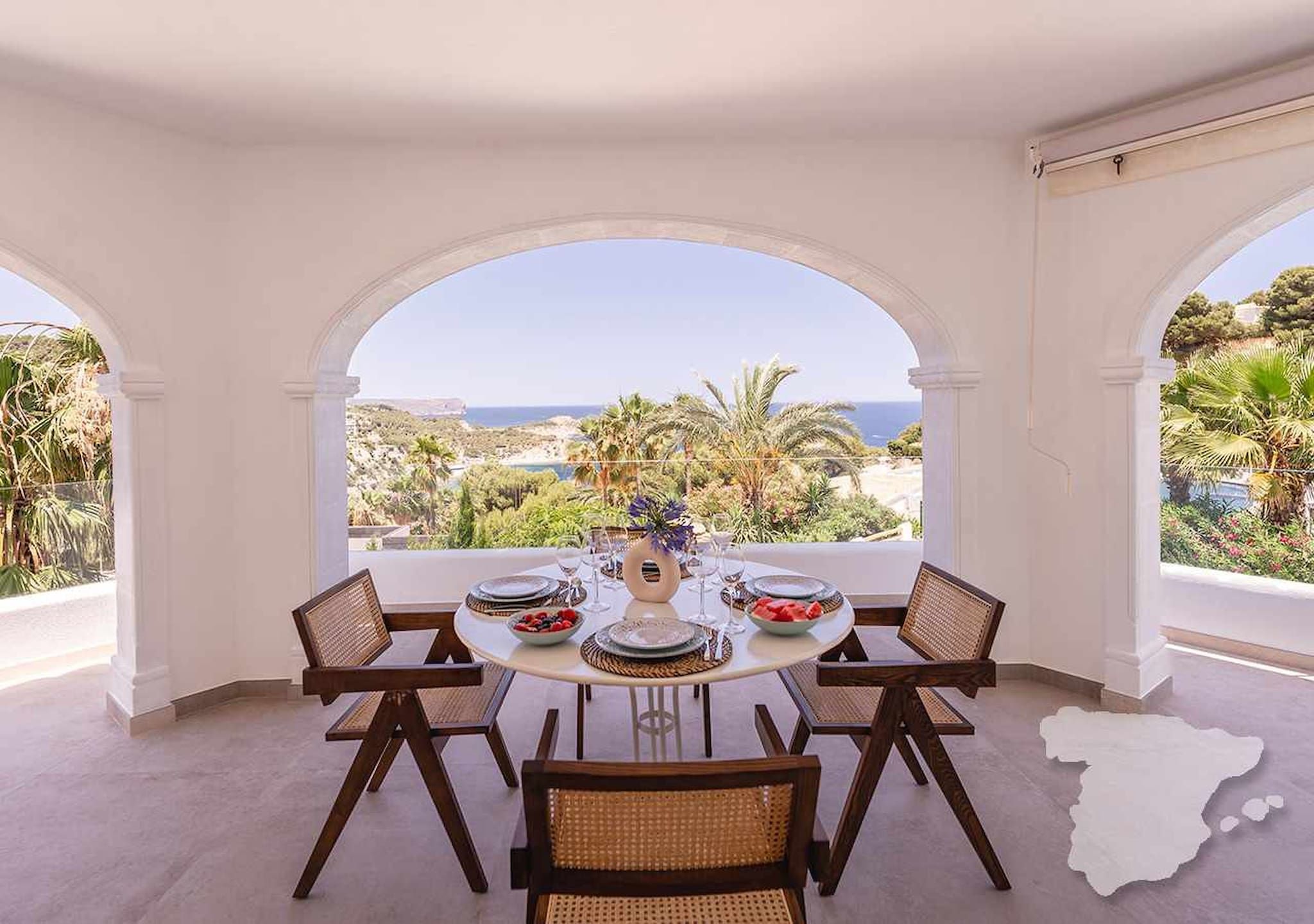 Un coin repas avec une table dressée pour six personnes, donnant sur un paysage côtier.
