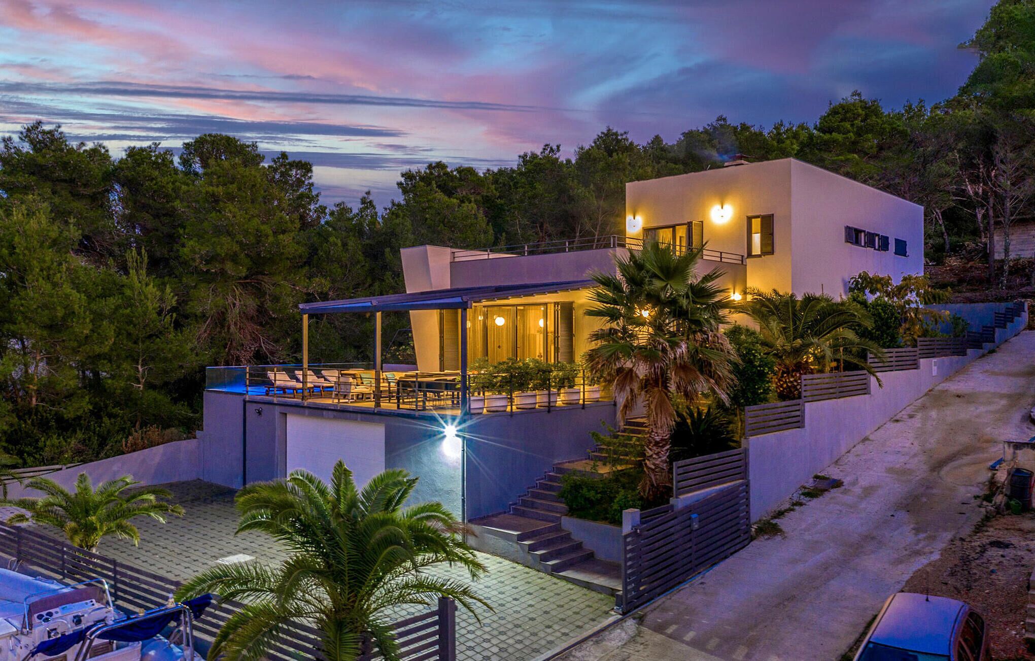 Et moderne hus med to etager, et overdækket udeområde, en swimmingpool og en trappe op til øvre plan.