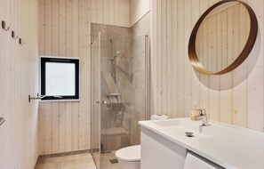 Experience a sleek bathroom with a round mirror, glass door, and handheld showerhead.