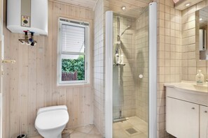 Ein Badezimmer mit Toilette, einer Dusche in Glaswand, einem Fenster mit Jalousien und einer gefliesten Wand.