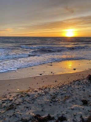 Ein Strand mit Wellen, einem Sonnenuntergang und verstreuten Seetang.